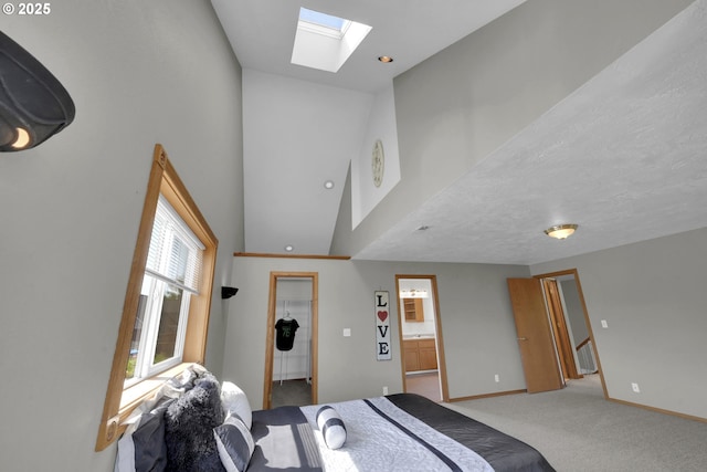 carpeted bedroom with ensuite bath, baseboards, a towering ceiling, a skylight, and a spacious closet