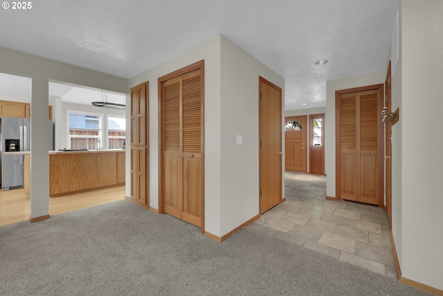 hallway with baseboards and light colored carpet