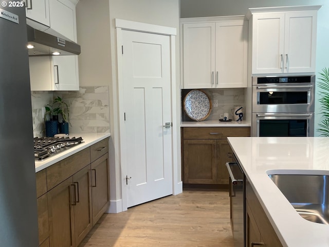 7839 SW Thornbridge Ter Unit 10, Beaverton, OR 97007 - kitchen featuring appliances with stainless steel finishes, light wood-style floors, tasteful backsplash, and light countertops