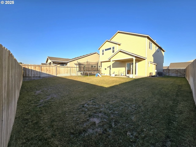 back of house featuring central AC, a trampoline, and a lawn