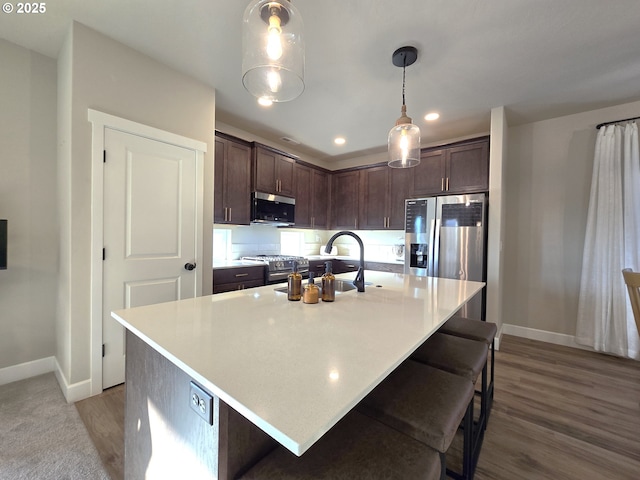 kitchen featuring sink, decorative light fixtures, dark brown cabinets, a center island with sink, and appliances with stainless steel finishes