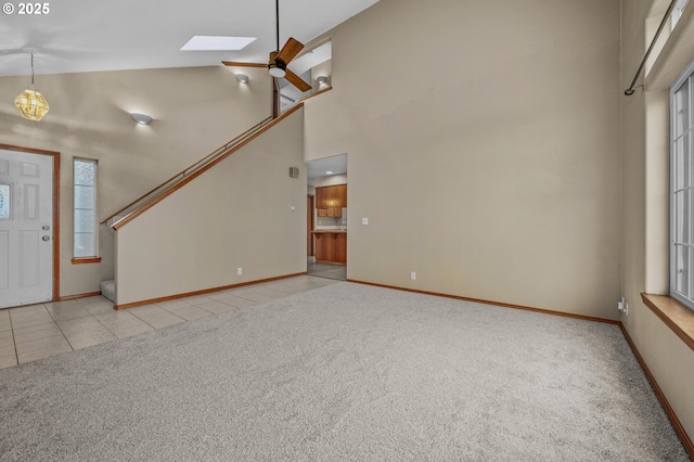 entryway featuring baseboards, high vaulted ceiling, a skylight, tile patterned floors, and carpet flooring