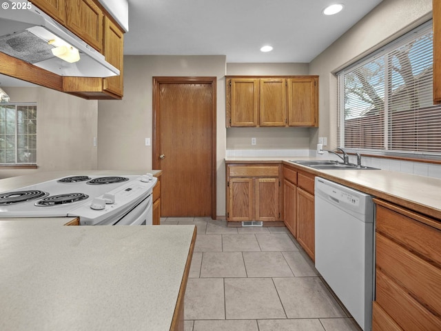 kitchen featuring light countertops, under cabinet range hood, a sink, and white appliances