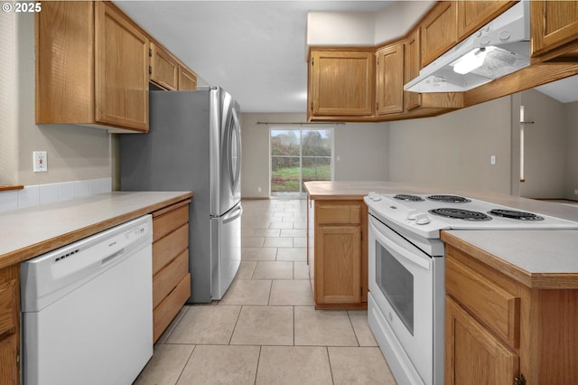 kitchen with white appliances, light tile patterned flooring, light countertops, under cabinet range hood, and a center island