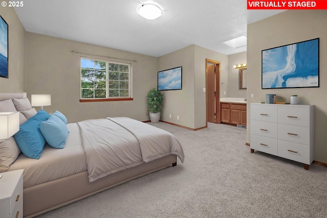 bedroom featuring baseboards, a skylight, ensuite bathroom, a textured ceiling, and light colored carpet