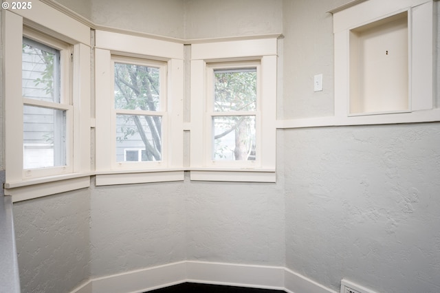 unfurnished room with a healthy amount of sunlight, a baseboard heating unit, and a textured wall