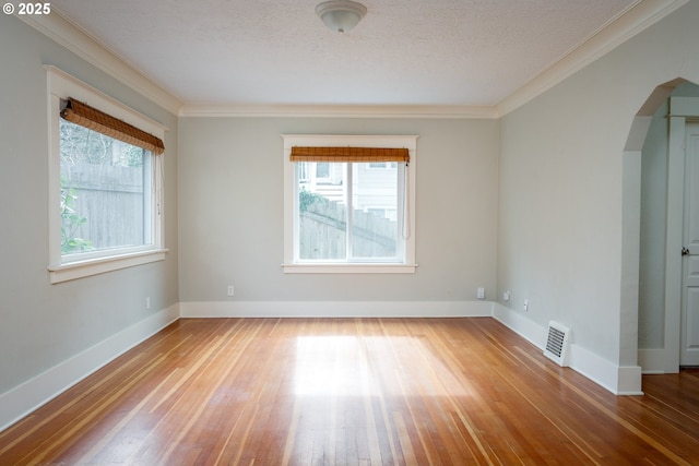 empty room with baseboards, hardwood / wood-style floors, visible vents, and crown molding