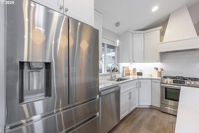 kitchen with white cabinetry, decorative light fixtures, premium range hood, sink, and appliances with stainless steel finishes