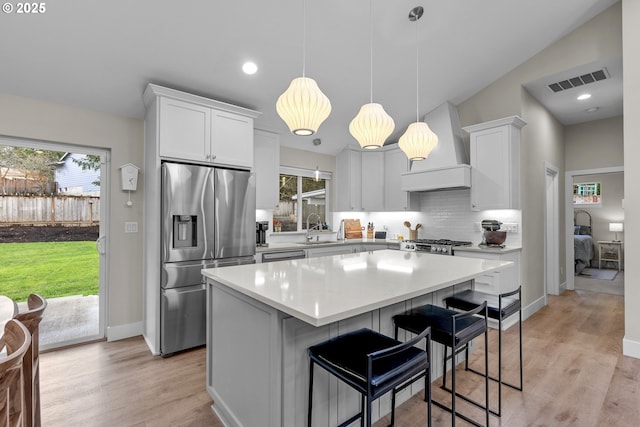 kitchen with white cabinetry, a kitchen island, stainless steel appliances, and custom range hood