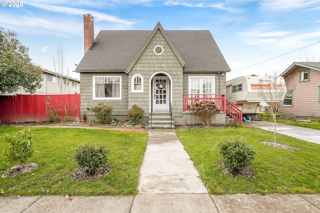 view of front of property featuring a shingled roof, a chimney, fence, and a front yard