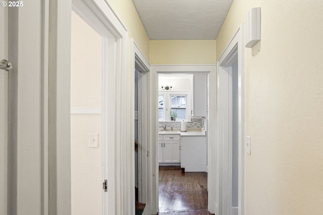 corridor with dark wood finished floors, a sink, and a textured ceiling