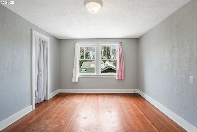 unfurnished room with a textured wall, a textured ceiling, baseboards, and wood finished floors