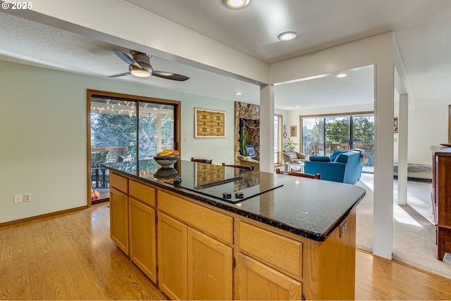 kitchen featuring ceiling fan, light hardwood / wood-style floors, a kitchen island, black electric cooktop, and dark stone counters