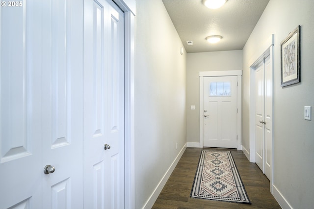 doorway featuring baseboards, a textured ceiling, and dark wood-type flooring