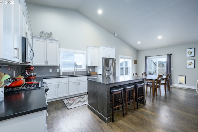 kitchen featuring appliances with stainless steel finishes, a sink, dark countertops, white cabinetry, and high vaulted ceiling