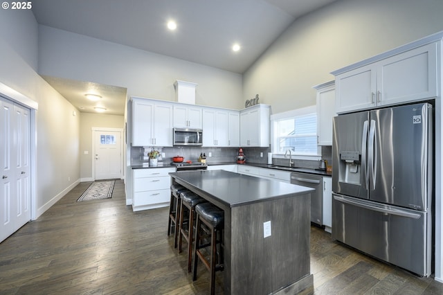 kitchen featuring stainless steel appliances, a sink, high vaulted ceiling, dark countertops, and a center island