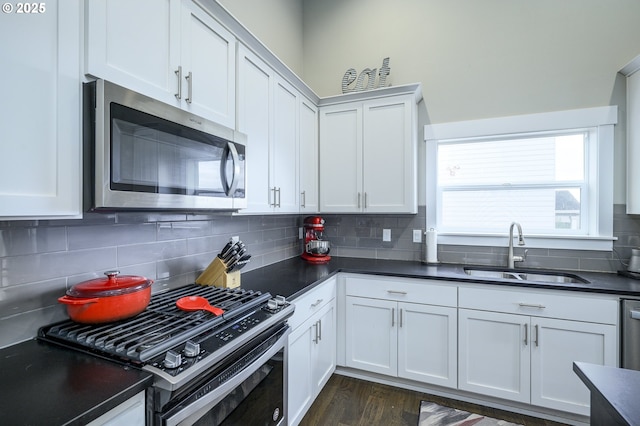 kitchen with appliances with stainless steel finishes, a sink, dark countertops, backsplash, and white cabinetry