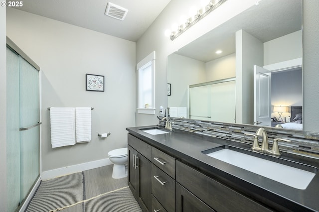 bathroom with baseboards, a stall shower, toilet, double vanity, and ensuite bath