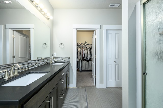 full bathroom with double vanity, a spacious closet, and tasteful backsplash