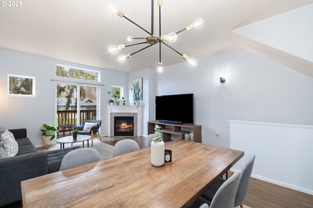 dining space with wood finished floors, baseboards, a tile fireplace, vaulted ceiling, and a chandelier