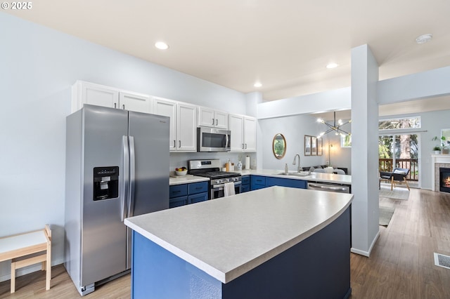 kitchen with a sink, wood finished floors, appliances with stainless steel finishes, light countertops, and a chandelier