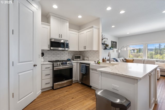 16615 SE Sunshower Pl, Happy Valley, OR 97086 - kitchen featuring appliances with stainless steel finishes, open floor plan, light wood finished floors, tasteful backsplash, and a peninsula