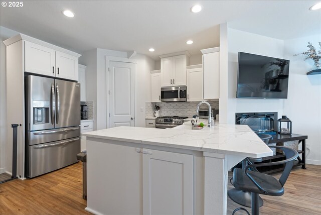 16615 SE Sunshower Pl, Happy Valley, OR 97086 - kitchen with appliances with stainless steel finishes, white cabinets, light wood-style floors, light stone countertops, and decorative backsplash