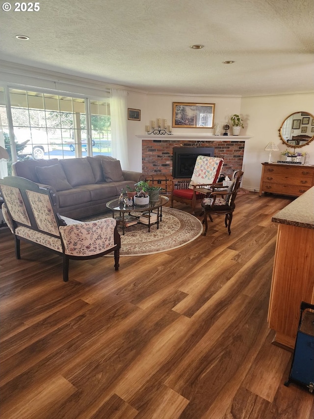 living area featuring a brick fireplace, a textured ceiling, dark wood-type flooring, and ornamental molding