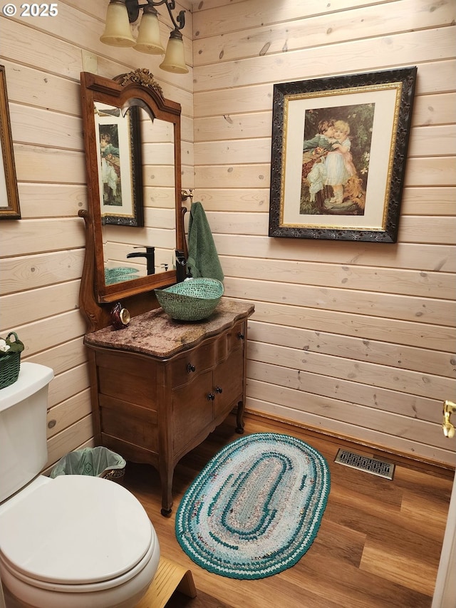 bathroom with wood walls, visible vents, toilet, and wood finished floors