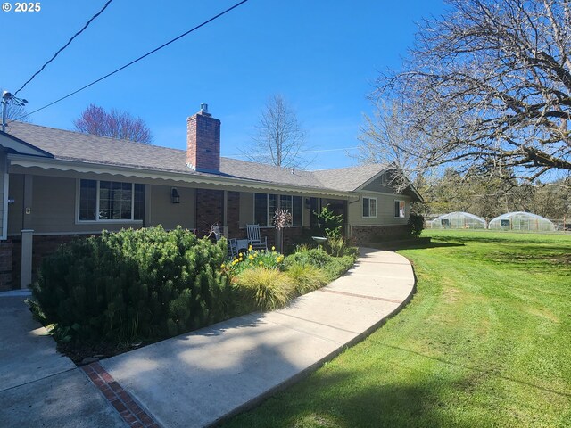 exterior space with a shingled roof, brick siding, a chimney, and a front lawn