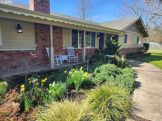 view of front of property featuring brick siding, covered porch, a chimney, and a shingled roof