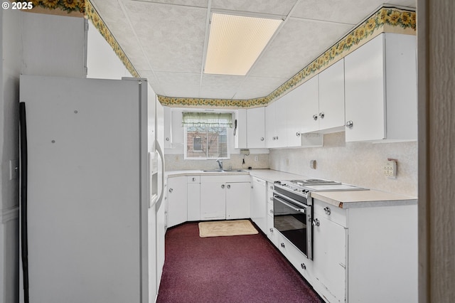 kitchen featuring light countertops, decorative backsplash, white cabinets, a sink, and white appliances