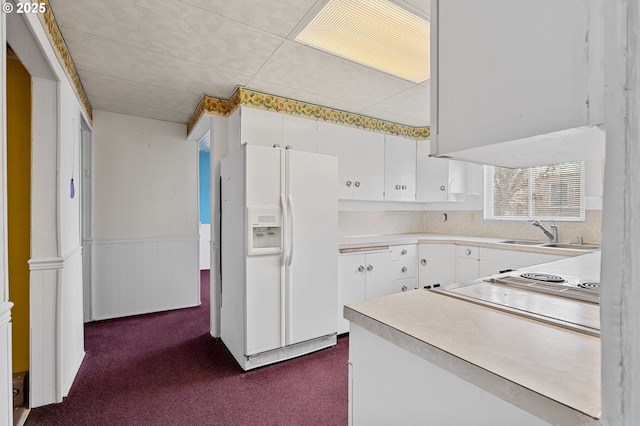 kitchen featuring white refrigerator with ice dispenser, light countertops, dark carpet, white cabinetry, and a sink