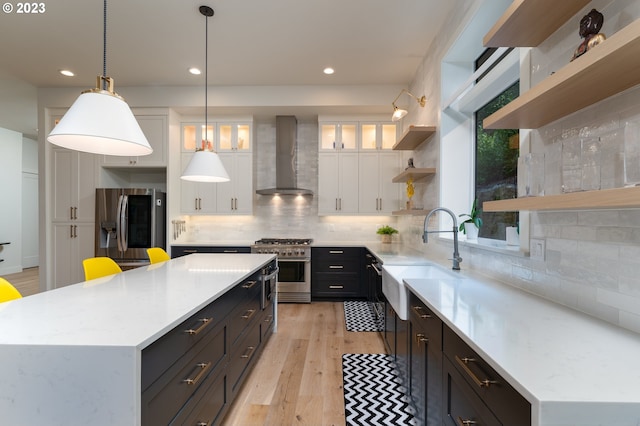 kitchen featuring decorative light fixtures, stainless steel appliances, white cabinets, tasteful backsplash, and wall chimney exhaust hood