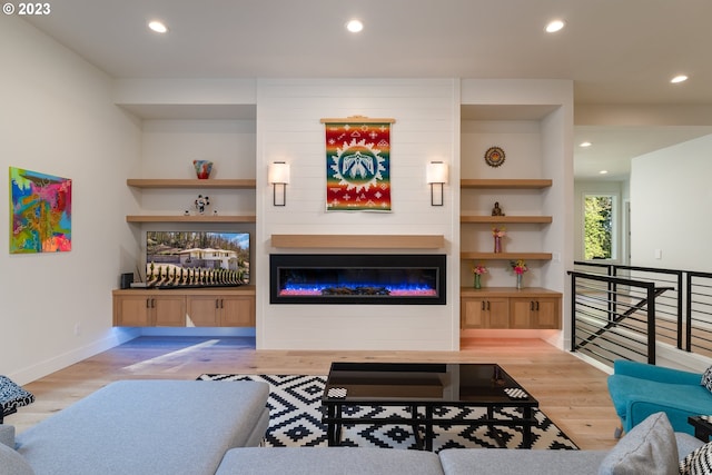 living room with built in features, a fireplace, and light wood-type flooring