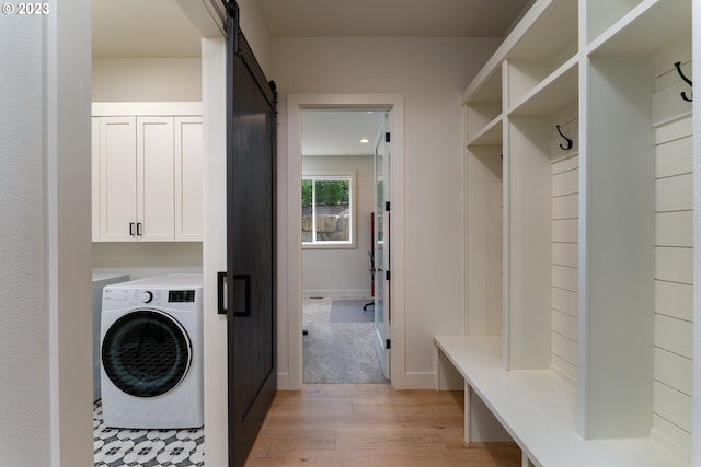 laundry room featuring a barn door, cabinets, washer and dryer, and light hardwood / wood-style flooring