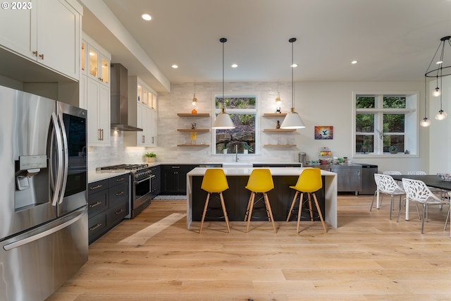 kitchen with wall chimney range hood, white cabinetry, light hardwood / wood-style floors, and stainless steel appliances