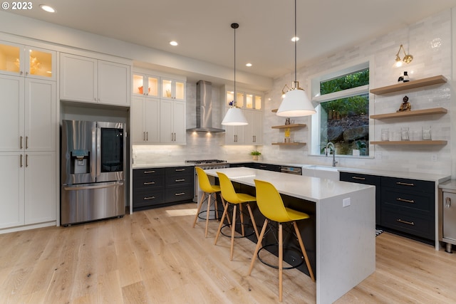 kitchen featuring appliances with stainless steel finishes, light hardwood / wood-style floors, white cabinets, wall chimney range hood, and pendant lighting