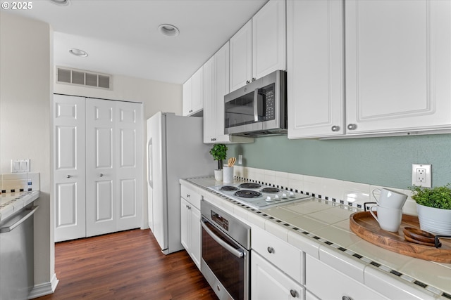 kitchen with tile counters, appliances with stainless steel finishes, visible vents, white cabinetry, and dark wood-style floors