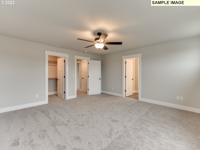 unfurnished bedroom with ceiling fan, a walk in closet, light colored carpet, and a closet