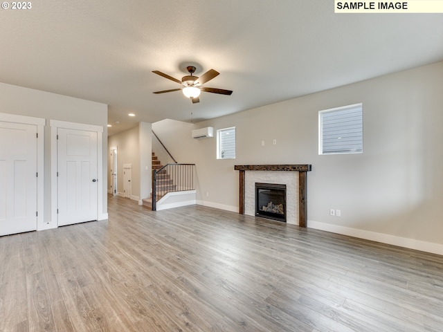 unfurnished living room featuring a wall mounted air conditioner, ceiling fan, and light hardwood / wood-style flooring