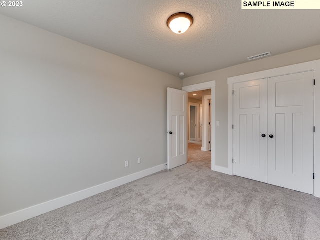 unfurnished bedroom featuring a closet, light carpet, and a textured ceiling