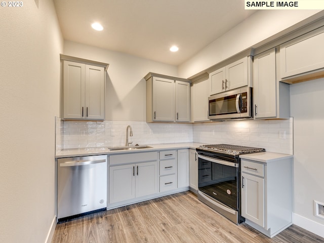 kitchen with backsplash, sink, light wood-type flooring, and stainless steel appliances