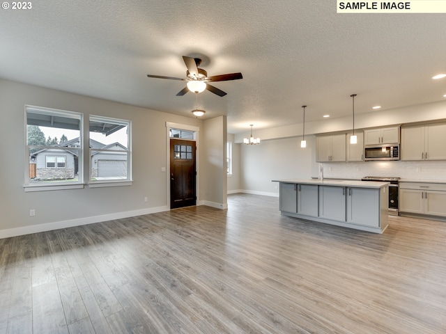 kitchen with an island with sink, pendant lighting, light hardwood / wood-style floors, appliances with stainless steel finishes, and gray cabinetry