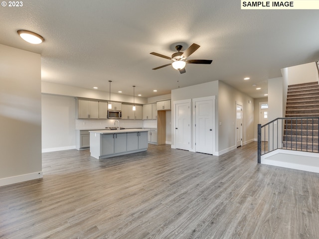 unfurnished living room with ceiling fan, sink, light hardwood / wood-style floors, and a textured ceiling