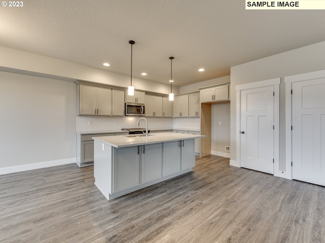 kitchen featuring pendant lighting, light wood-type flooring, tasteful backsplash, a kitchen island with sink, and gray cabinets