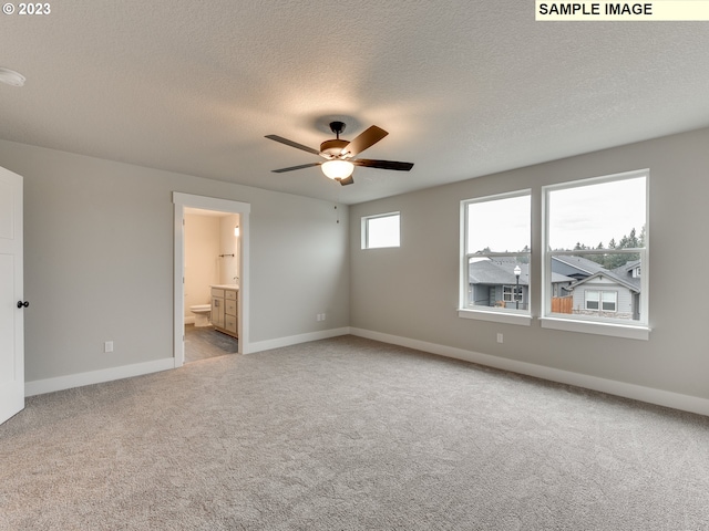 unfurnished bedroom with a textured ceiling, ensuite bath, ceiling fan, and light colored carpet