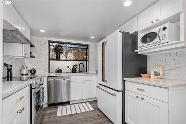 kitchen with a sink, under cabinet range hood, appliances with stainless steel finishes, white cabinetry, and dark wood-style flooring