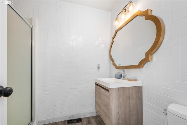 full bath featuring vanity, visible vents, an enclosed shower, tile walls, and toilet