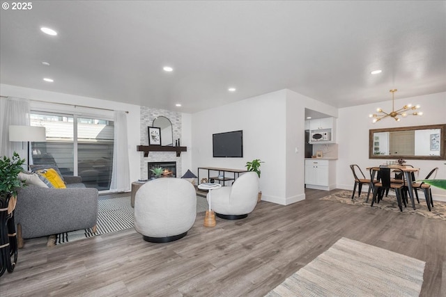 living room featuring a stone fireplace, recessed lighting, light wood-type flooring, and an inviting chandelier